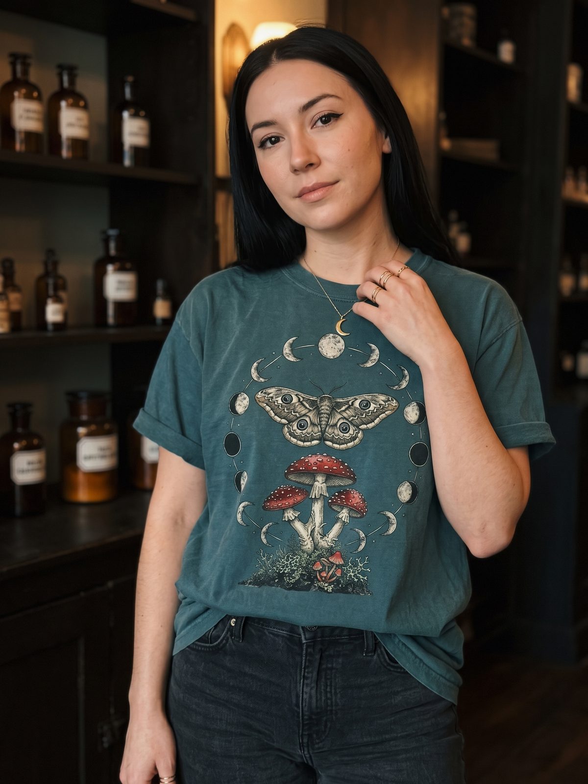 Woman in an apothecary wearing the Moon Phase Moth & Mushroom tee
